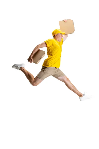 Joven repartidor de uniforme amarillo corriendo para entregar el pedido aislado sobre fondo blanco. Concepto de conveniencia, velocidad, comodidad, seguridad, servicio. — Foto de Stock