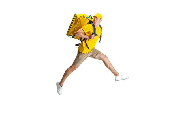 El joven repartidor de uniforme amarillo se apresura a entregar el pedido aislado sobre fondo blanco. Concepto de conveniencia, velocidad, comodidad, seguridad, servicio. — Foto de Stock