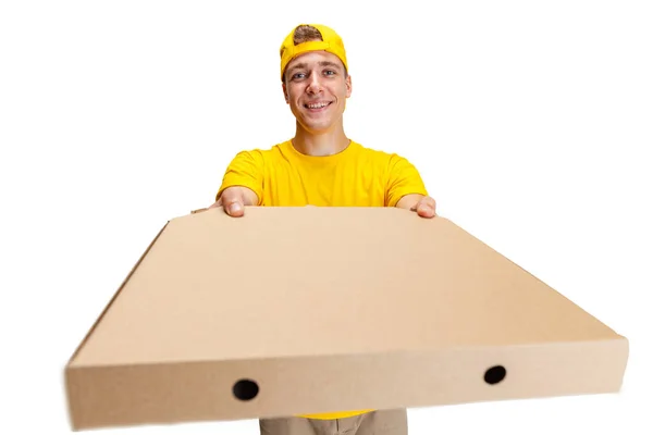 Primer plano joven repartidor en uniforme amarillo con caja de papel con pizza aislada sobre fondo blanco. Concepto de conveniencia, velocidad, comodidad, seguridad, servicio. — Foto de Stock