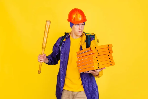 Комічний портрет молодого чоловіка, хлопця доставки в уніформі ізольовано на жовтому студійному фоні. Концепція гумору, безпеки, служіння. Додаткові кольори — стокове фото