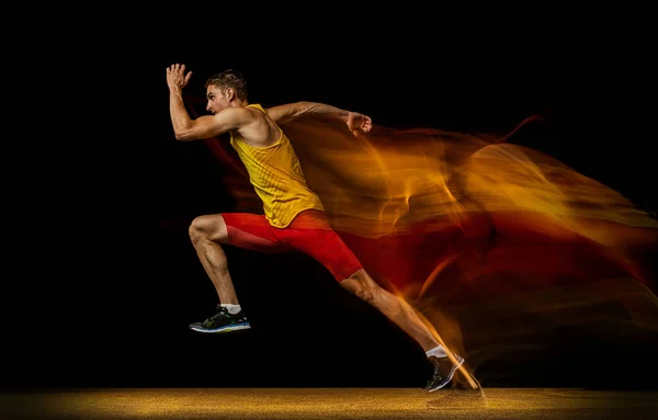 Retrato de jovem, atleta profissional masculino, corredor em movimento e ação isolado em fundo escuro. Efeito estroboscópio. — Fotografia de Stock