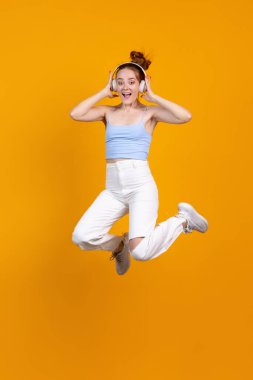Sarı stüdyo arka planında izole bir şekilde atlayan genç kızın dikey görüntüsü. Günlük giysiler içinde kadın manken. İnsan duyguları kavramı, doğal güzellik, gençlik