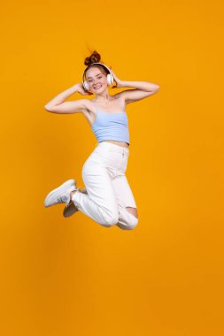 Sarı stüdyo arka planında izole bir şekilde atlayan genç kızın dikey görüntüsü. Günlük giysiler içinde kadın manken. İnsan duyguları kavramı, doğal güzellik, gençlik