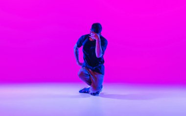 Modern dans tarzı. Hip hop, break dans, hareketli dans, koyu renk kıyafetler içinde hareket parlak mor arka planda neon ışıklı dans salonunda izole edilmiş..