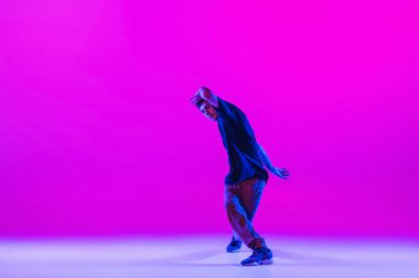 Dans eden adamın portresi, break dansçı, modern kıyafetler içinde hareket parlak mor arka planda neon ışıklı dans salonunda izole edilmiş..