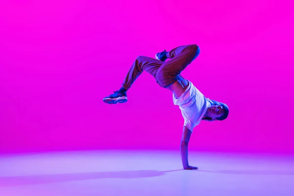 Een jonge stijlvolle man, breakdance danser training in moderne kleding geïsoleerd over heldere magenta achtergrond in de danszaal in neon licht. — Stockfoto