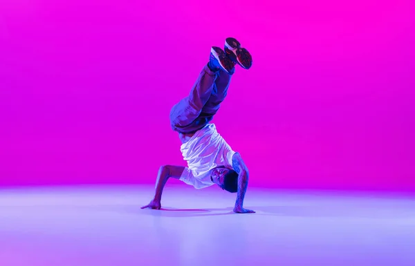 Een jonge stijlvolle man, breakdance danser training in moderne kleding geïsoleerd over heldere magenta achtergrond in de danszaal in neon licht. — Stockfoto