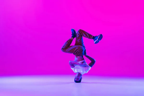 Portret van een jonge man, breakdance danseres die solo danst in moderne kleding geïsoleerd over een heldere magenta achtergrond in de danszaal in neon licht. — Stockfoto