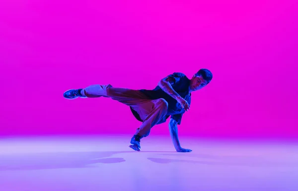 Jonge stijlvolle man, hip-hop danser dansen solo in moderne kleding geïsoleerd over heldere magenta achtergrond in danszaal in neon licht. — Stockfoto