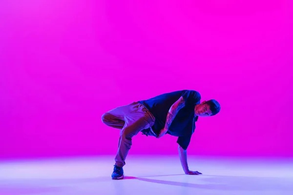Een dansende man, break danser in actie, beweging in moderne kleren geïsoleerd over heldere magenta achtergrond in danszaal in neon licht. — Stockfoto