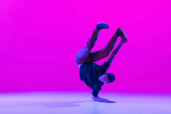 Jovem homem elegante, dançarino de hip-hop dançando sozinho em roupas modernas isoladas sobre fundo magenta brilhante no salão de dança em luz de néon. — Fotografia de Stock