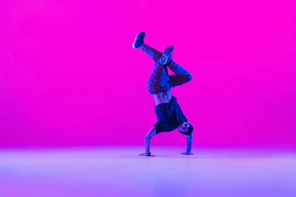Retrato de homem dançando, break dancer em ação, movimento em roupas modernas isoladas sobre fundo magenta brilhante na sala de dança em luz de néon. — Fotografia de Stock