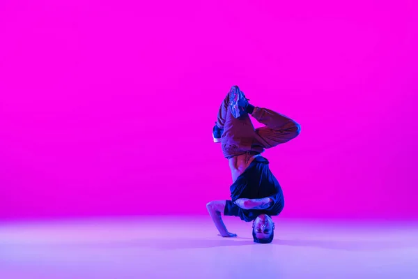 Portret van een jonge man, breakdance danseres die solo danst in moderne kleding geïsoleerd over een heldere magenta achtergrond in de danszaal in neon licht. — Stockfoto