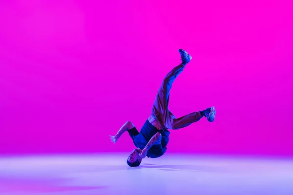 Retrato de jovem, dançarino de break-dance dançando sozinho em roupas modernas isoladas sobre fundo magenta brilhante no salão de dança em luz de néon. — Fotografia de Stock