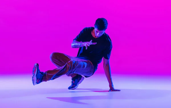 Portret van dansende man, breakdanser in actie, beweging in moderne kleding geïsoleerd over heldere magenta achtergrond in danszaal in neon licht. — Stockfoto