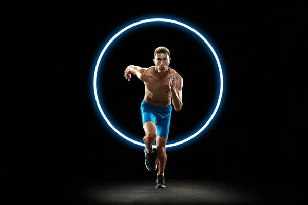 Dynamický, energický. Mladý běžec v akci na černém pozadí se zářivým kruhem. Abstraktní desing, koncept aktivního životního stylu, krása, pohyb ve sportu — Stock fotografie