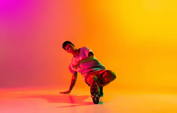 Pełna długość portret młodego stylowego mężczyzny, break dance tancerz w casual ubrania odizolowane nad gradient różowy żółty tło w sali tanecznej w neonowym świetle. — Zdjęcie stockowe