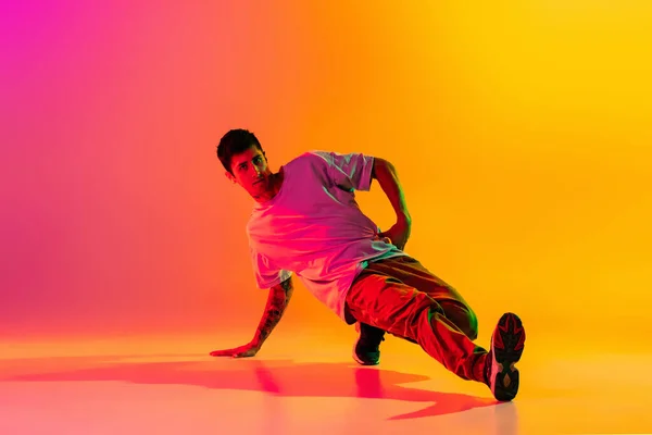 Desempenho a solo. Jovem, dança break dançarino ptacticing em roupas casuais isolado sobre gradiente rosa fundo amarelo no salão de dança em luz de néon. — Fotografia de Stock