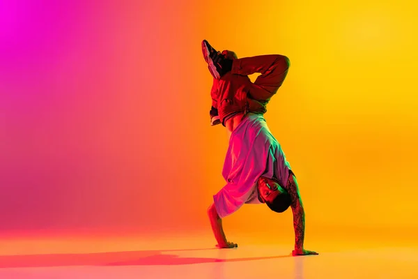 Retrato de jovem homem elegante, break dança dançarina formação em roupas casuais isolado sobre gradiente rosa fundo amarelo na sala de dança em luz de néon. — Fotografia de Stock