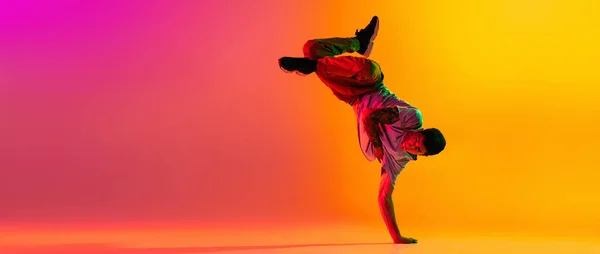 Folheto com jovem homem elegante, break dança treinamento dançarino em roupas casuais isolado sobre gradiente rosa fundo amarelo na sala de dança em luz de néon. — Fotografia de Stock