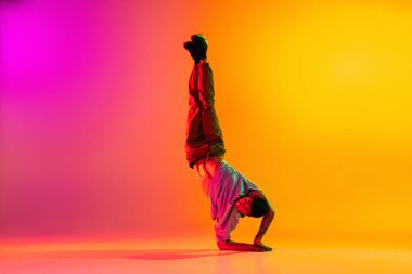 Beyaz adam, break dans yapan dansçı gündelik kıyafetlerle dans ediyor. Neon ışıklarıyla dans salonundaki sarı arka planda izole edilmiş..