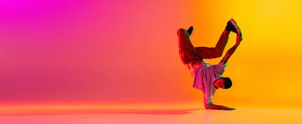 Flyer met jonge stijlvolle man, breakdance danser training in casual kleding geïsoleerd over verloop roze gele achtergrond in danszaal in neon licht. — Stockfoto