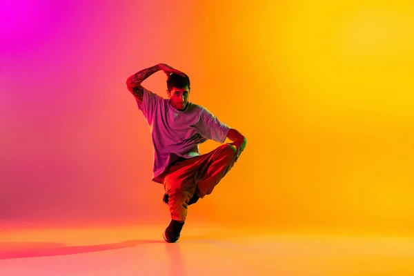 Em acção. Jovem, dança break dançarino ptacticing em roupas casuais isolado sobre gradiente rosa fundo amarelo no salão de dança em luz de néon. — Fotografia de Stock