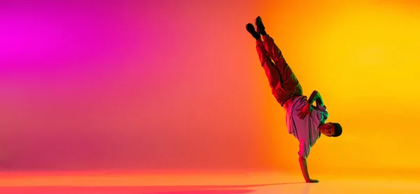 Flyer met jonge stijlvolle man, breakdance danser training in casual kleding geïsoleerd over verloop roze gele achtergrond in danszaal in neon licht. — Stockfoto