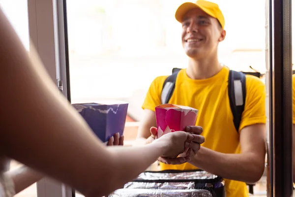 Jovem entregador em uniforme amarelo entrega ordem para clientes, clientes, compradores. Trabalho, carreira, conceito de profissões diferentes. Idéia de conveniência, velocidade, conforto, segurança, serviço. — Fotografia de Stock