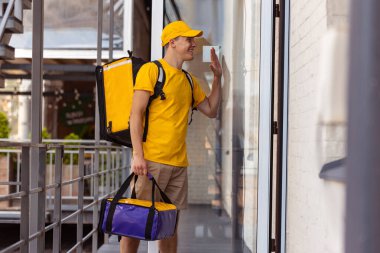 Sarı üniformalı genç teslimatçı müşterilere, müşterilere, alıcılara sipariş veriyor. İş, kariyer, farklı meslekler. Konfor fikri, hız, konfor, güvenlik, hizmet.