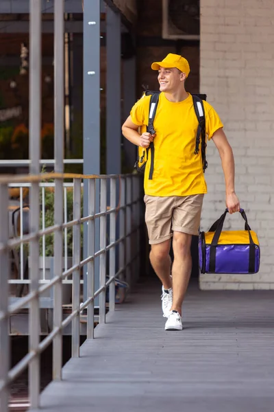 Jovem entregador em uniforme amarelo entrega ordem para clientes, clientes, compradores. Trabalho, carreira, conceito de profissões diferentes. Idéia de conveniência, velocidade, conforto, segurança, serviço. — Fotografia de Stock