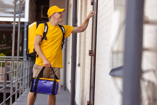 Joven repartidor en uniforme amarillo entrega orden a clientes, clientes, compradores. Trabajo, carrera, diferentes profesiones concepto. Idea de conveniencia, velocidad, comodidad, seguridad, servicio. — Foto de Stock