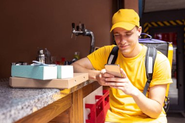 Sarı üniformalı genç teslimatçı müşterilere, müşterilere, alıcılara sipariş veriyor. İş, kariyer, farklı meslekler. Konfor fikri, hız, konfor, güvenlik, hizmet.