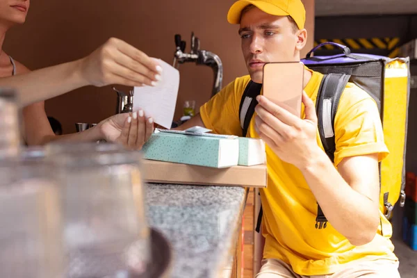 Jovem entregador de uniforme amarelo pegando ordem para clientes, clientes, compradores. Trabalho, carreira, conceito de profissões diferentes. Idéia de conveniência, velocidade, conforto, segurança, serviço. — Fotografia de Stock