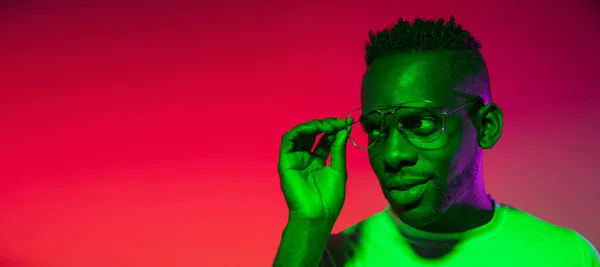 Image créative de jeune homme africain en vêtements décontractés isolé sur fond de studio de couleur rouge au néon, filtre. Concept d'émotions humaines, expression faciale, jeunesse, sentiments, publicité. — Photo