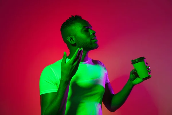 Imagem criativa do jovem africano em roupas casuais isoladas em fundo estúdio de cor vermelha em luz de néon, filtro. Conceito de emoções humanas, expressão facial, juventude, sentimentos, ad. — Fotografia de Stock