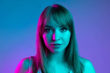 Mavi stüdyo arka planında neon ışık filtresiyle izole edilmiş güzel bir kızın yakın plan portresi. İnsan duyguları kavramı, yüz ifadesi, gençlik, satış, reklam.