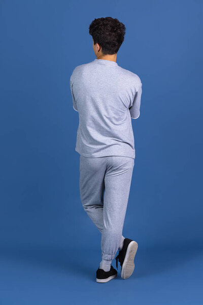 Back view of young curly man standing isolated over blue, navy studio background. Copyspace for ad, design. Concept of human emotions, fashion, beauty, youth