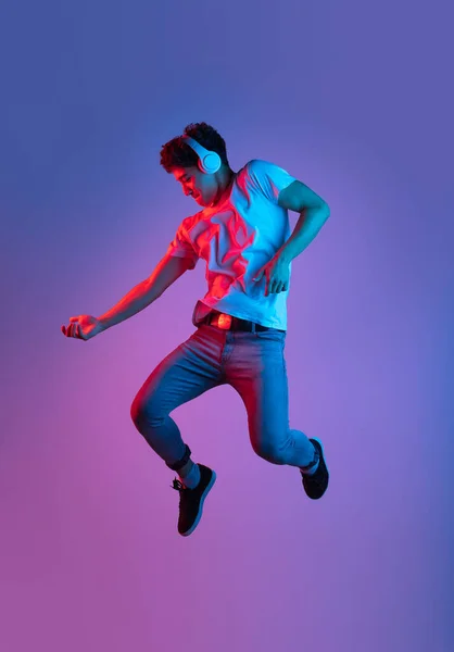 Stijlvolle jonge Aziatische man springen geïsoleerd over lila kleur studio achtergrond in roze neon licht. Concept van menselijke emoties, mode, schoonheid, jeugd — Stockfoto
