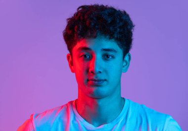 Genç kıvırcık adamın yakın plan portresi. Pembe neon ışıkta eflatun rengi stüdyo arka planında izole edilmiş. İnsan duyguları, moda, güzellik, gençlik kavramı