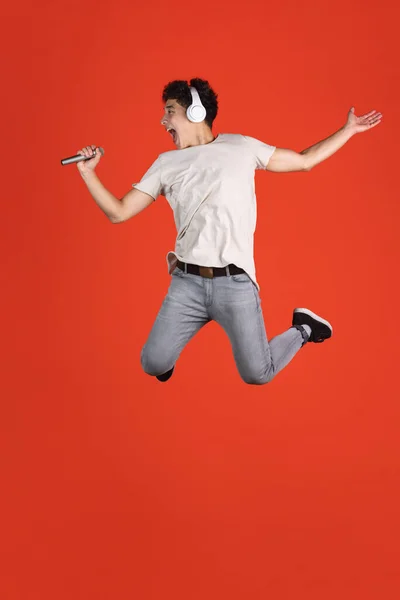 Et helaftens portrett av en ung mann som hopper isolert over rød studiobakgrunn med opphavsrom for reklame. Konseptet menneskelige følelser, mote, skjønnhet, ungdom – stockfoto