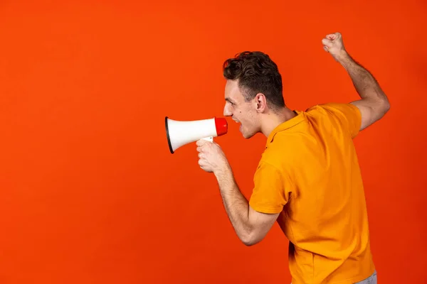 Porträt eines jungen kaukasischen Mannes, der isoliert auf orangefarbenem Studiohintergrund ein Megafon anbrüllt. Konzept menschlicher Emotionen, Mimik, Jugend, Gefühle, Werbung. — Stockfoto