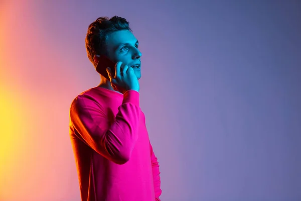Halva längden porträtt av ung vit man med telefon, gadget isolerad lila färg studio bakgrund i rosa neon ljusfilter. Begreppet mänskliga känslor, ansiktsuttryck, ungdomar, känslor, annons. — Stockfoto