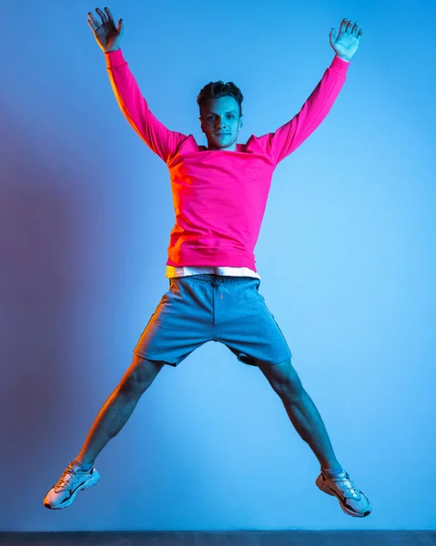 Full length portret van jonge knappe man springen geïsoleerde paarse kleur studio achtergrond in roze neon lichtfilter. Concept van menselijke emotie, gezichtsuitdrukkingen, jeugd, gevoelens, ad. — Stockfoto