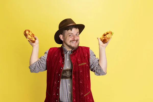 Boldog mosolygós férfi, hagyományos bajor jelmezben, finom perecekkel, sárga háttérrel elszigetelve. Nemzeti konyha, ünnepek, hagyományok — Stock Fotó