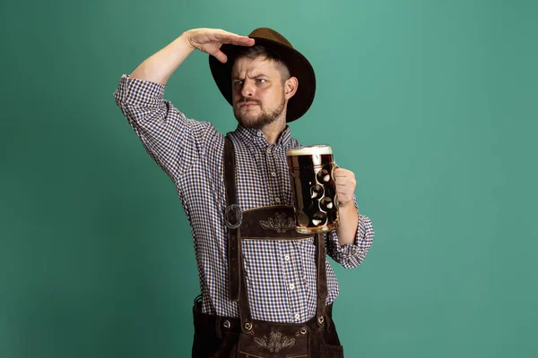 Retrato de hombre barbudo en traje bávaro tradicional con un litro de cerveza oscura aislada sobre fondo verde. Festival de octubre, Concepto del festival — Foto de Stock