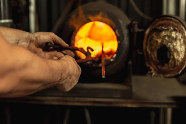 Close-up werken krachtige handen van mannelijke smid het maken van rood heet metaal in oven, hoorn. Werkproces van het verwarmen van metaal in smederij. Begrip arbeid, retro beroepen, familiebedrijf — Stockfoto