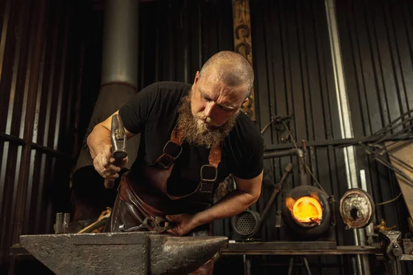 Sakallı adam, demirci demircideki erimiş metali havai fişeklerle elle dövüyor. Çalışma anlayışı, geçmişe dönük meslekler, aile meslekleri — Stok fotoğraf