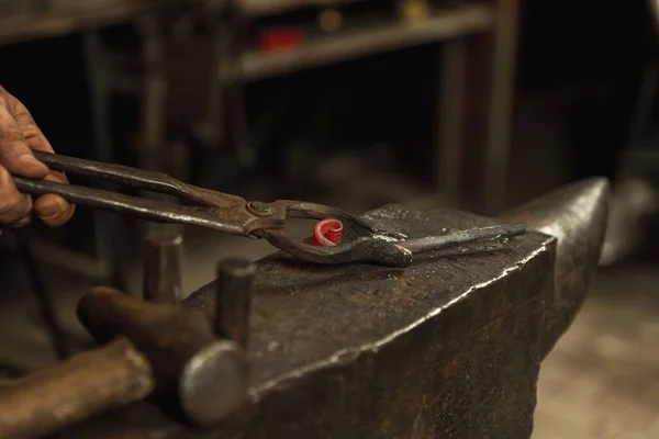 Egy férfi kovács közeli kezei kovácsolnak vasat egy kovácsban. Kalapács, vörös forró fém és üllő. A munka fogalma, retro szakmák — Stock Fotó