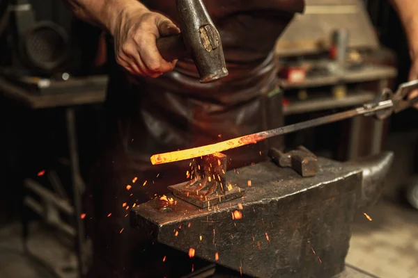 Mãos poderosas e fechadas do ferreiro forjam um produto de ferro num ferreiro. Martelo, metal quente vermelho e bigorna. Conceito de trabalho, profissões retro — Fotografia de Stock